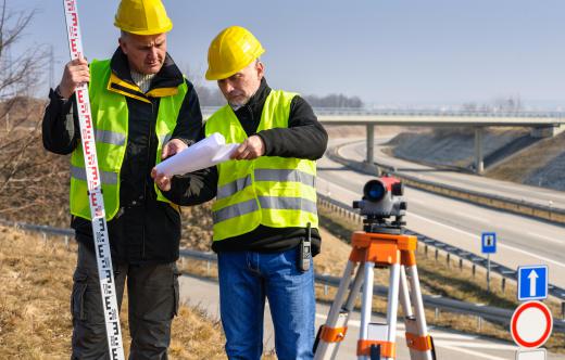 A surveyor trainee assists the main surveyor at a construction job site or office position.