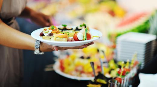 A buffet set up by a party caterer may include a vegetarian entree as well as fresh fruit and salad ingredients.